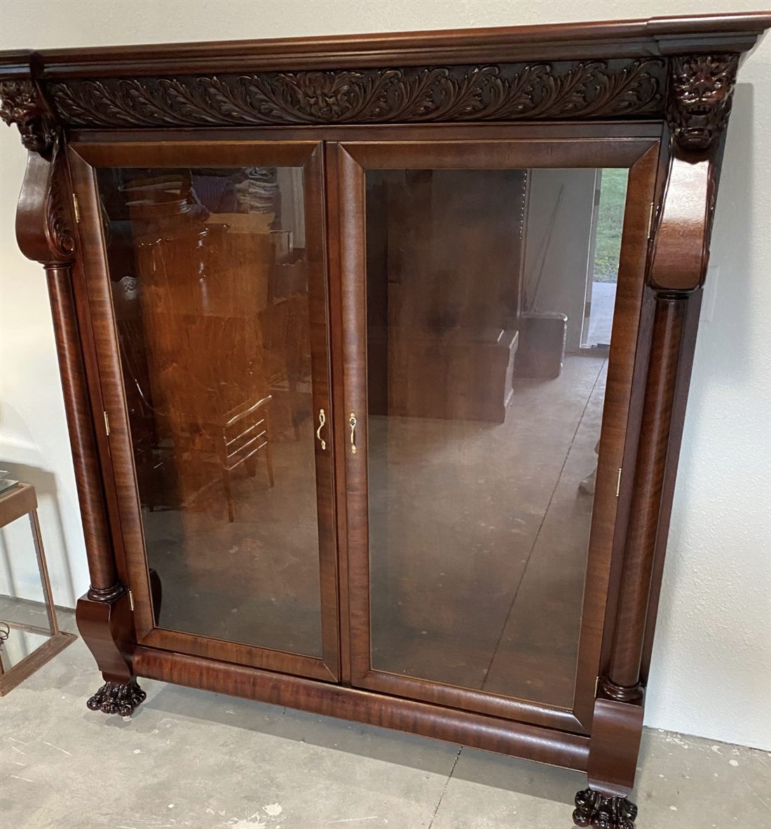 A restored mahogany bookcase with a carved lions-head crown and glass doors
